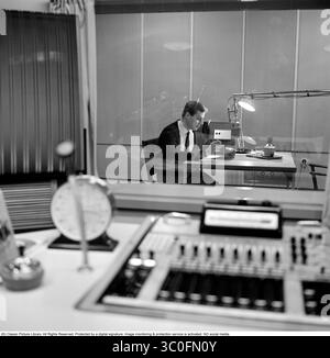 Radiostudio aus den 1960er Jahren. Radiomoderator Klas Burling (1941–2023) im Studio vor dem Mikrofon, wenn er auf Sendung ist, aus dem Raum der Radiomoduzenten und Tontechniker durch das schalldichte Fenster, das sie voneinander trennt, gesehen. 1963 Stockfoto
