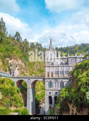 Atemberaubende Aussicht auf die Kirche Las Lajas, eine bemerkenswerte gotische Kirche, die auf einer Klippe erbaut wurde und von üppigen grünen Hügeln und einem blauen Himmel in Nariño, Kolumbien, umgeben ist. Stockfoto