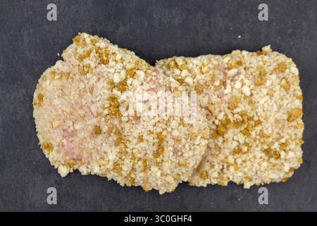 Rohes Hühnerschnitzel in Brotkrumen auf dem schwarzen Küchenbrett Stockfoto