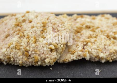Rohes Hühnerschnitzel in Brotkrumen auf dem schwarzen Küchenbrett Stockfoto