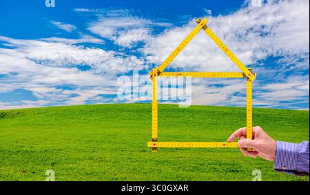Wohnen auf dem Land, Handschuh in der Natur ein Meterstab ist gefaltet wie ein Haus und wird mit der Hand vor einer unberührte Landschaft, Handschuh in der N Stockfoto