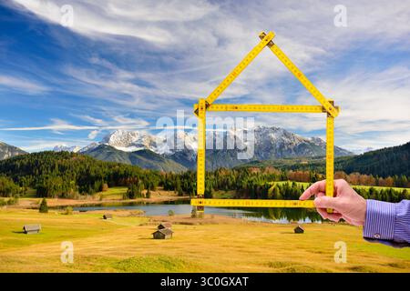 Wohnen auf dem Land, Handschuh in der Natur ein Meterstab ist gefaltet wie ein Haus und wird mit der Hand vor einer unberührte Landschaft, Handschuh in der N Stockfoto