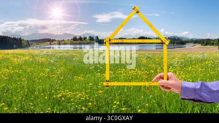 Wohnen auf dem Land, Handschuh in der Natur ein Meterstab ist gefaltet wie ein Haus und wird mit der Hand vor einer unberührte Landschaft, Handschuh in der N Stockfoto