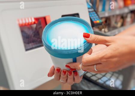 Junge Frau scannt Plastikbehälter mit Haushaltschemikalien am Selbstkasse-Terminal im modernen Einzelhandel Stockfoto
