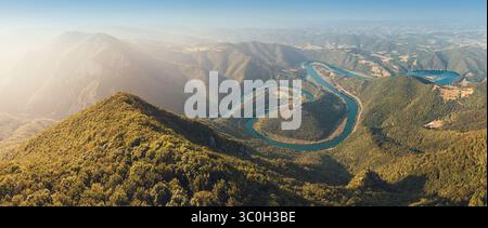 Aus der Vogelperspektive auf einen sich windenden Fluss, der durch üppige grüne Berge fließt und an einem Sommertag eine malerische Landschaft schafft Stockfoto