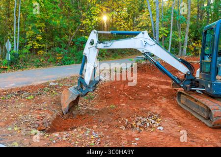 Ein Bagger gräbt aktiv Schmutzgräben entlang Schotterwegen mit Bäumen auf der Baustelle Stockfoto