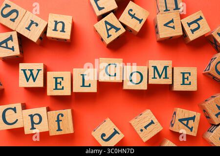 Wort Willkommen aus Holzwürfeln auf rotem Hintergrund, flach gelegen Stockfoto
