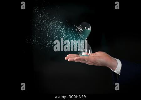 Die Zeit wird knapp. Sanduhr löst sich in der Hand des Menschen auf schwarzem Hintergrund auf, Nahaufnahme Stockfoto