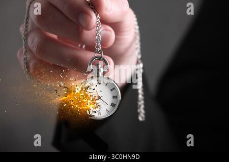 Die Zeit wird knapp. Taschenuhr löst sich in der Hand des Mannes auf grauem Hintergrund auf, Nahaufnahme Stockfoto