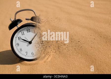Die Zeit wird knapp. Schwarzer Wecker löst sich in Sand auf Stockfoto