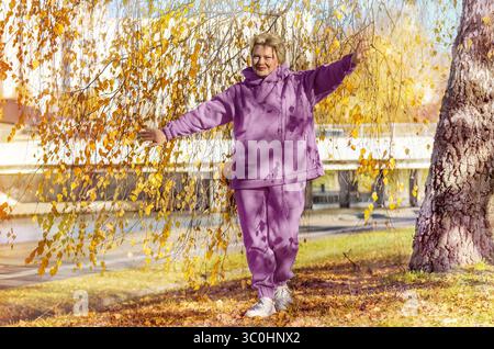 Reife Frau in rosa Hoodie oder Trainingsanzug, die im Herbstpark spazieren geht. Digitale Detox, Sport. Stockfoto