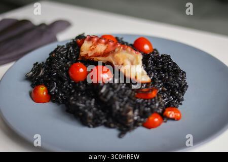 Nahaufnahme mit exotischem Meeresfrüchterisotto mit Oktopus und Tomaten, schwarzem Reisgericht für kulinarische Zwecke oder Menügestaltung. Stockfoto