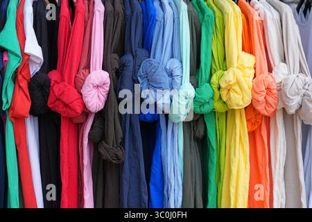 Bunte Leinenhemden mit hochgerollten Ärmeln, die an einem Regal hängen Stockfoto