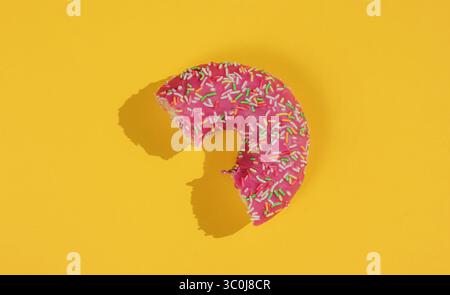 Pop Art minimalistisches Food Stillleben. Gebissener glasierter Donut auf gelbem Hintergrund. Modekonzept. Draufsicht Stockfoto