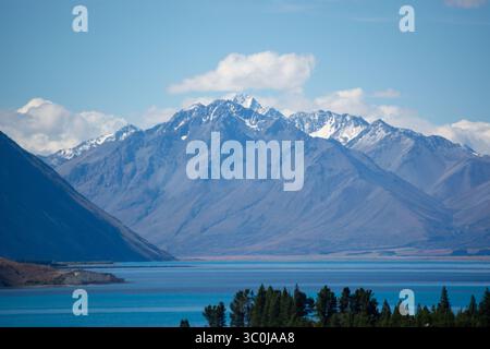 Eine atemberaubende Landschaft mit schneebedeckten Bergen, die majestätisch über einem ruhigen See ragen, umgeben von üppigem Grün und einem klaren blauen Himmel. Stockfoto