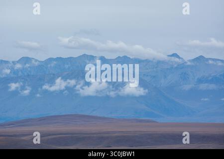 Eine ruhige Landschaft mit weit entfernten Bergen, die in Wolken gehüllt sind, mit einer weiten Ebene im Vordergrund. Die Szene vermittelt ein Gefühl von Ruhe und N Stockfoto
