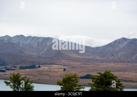 Eine ruhige Landschaft mit sanften Bergen unter bewölktem Himmel, mit einem ruhigen See im Vordergrund und karger Vegetation entlang der Küste. Stockfoto