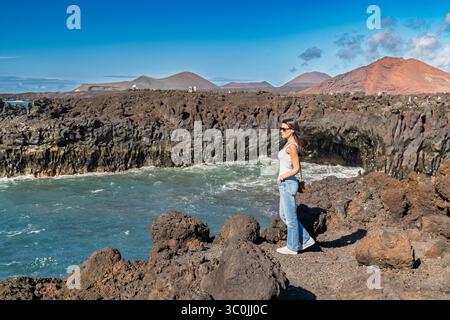 Eine junge Brünette genießt die dramatischen vulkanischen Klippen und den Blick auf das Meer in Los Hervideros und fängt die einzigartige und zerklüftete Küste der Insel ein Stockfoto