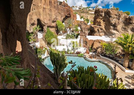Eine atemberaubende weiße Villa mit einem Pool, eingebettet zwischen roten vulkanischen Felsen, harmonisch in die dramatische natürliche Landschaft der Insel. Stockfoto