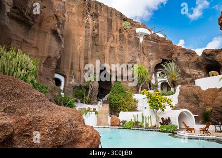 Eine atemberaubende weiße Villa mit einem Pool, eingebettet zwischen roten vulkanischen Felsen, harmonisch in die dramatische natürliche Landschaft der Insel. Stockfoto