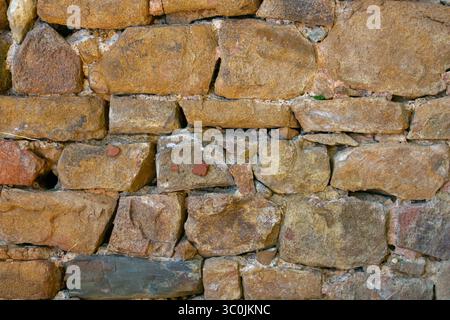 Eine alte Steinmauer zeigt eine Vielzahl von rauen, unregelmäßig geformten Felsen, die eine Mischung aus Erdtönen zeigen, die fest in einem natürlichen en stehen Stockfoto
