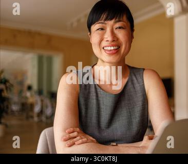 Porträt einer selbstbewussten Managerin mit überkreuzten Armen, die in die Kamera lächelt, während sie in einem modernen Büro arbeitet Stockfoto