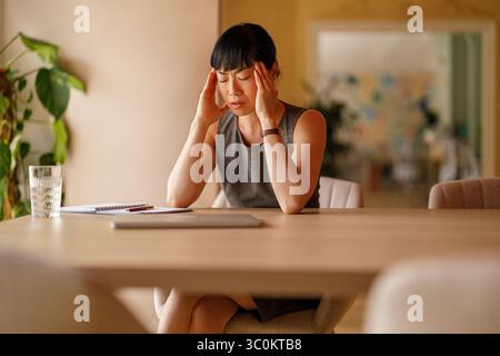 Gestresste Geschäftsfrau mit Kopf in Händen, die von der Arbeitsbelastung und den Terminen am Schreibtisch des Unternehmens überfordert ist Stockfoto