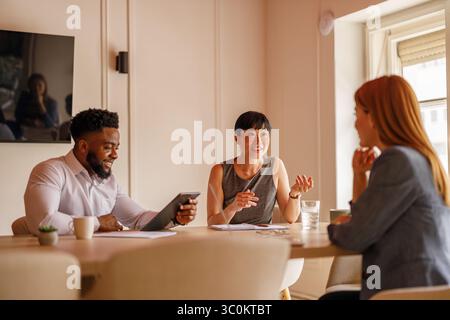 Geschäftskollegen mit digitalem Tablet und Dokumenten teilen ihre Ideen im Vorstandssitz während der Bürositzung Stockfoto