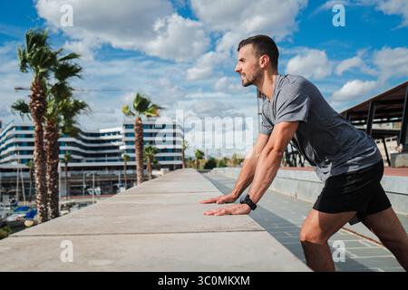 Konzentrierter Mann, der eine effektive Dehnungsübung durchführt, um die Flexibilität und die allgemeine sportliche Leistung zu verbessern, während er die Natur und die Umgebung genießt Stockfoto