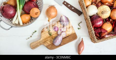 Schneidebrett, Sieb und Korb mit verschiedenen Zwiebelsorten auf weißem hölzernem Hintergrund, Ansicht von oben Stockfoto