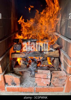 Flammen und glühende Glut in einem gemauerten Kamin mit brennenden Holzstämmen zum Grillen Stockfoto