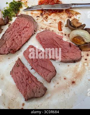 Geschnittenes gegrilltes Fleisch, das auf einem Teller serviert wird, typisch für brasilianische Grillgerichte im Rodizio-Stil, begleitet von Pilzen und Sauce. Stockfoto