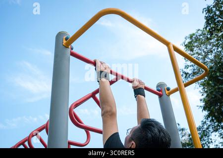 Ein Mann, der Klimmzüge auf der Stahlstange im Park macht. Rückansicht. Stockfoto