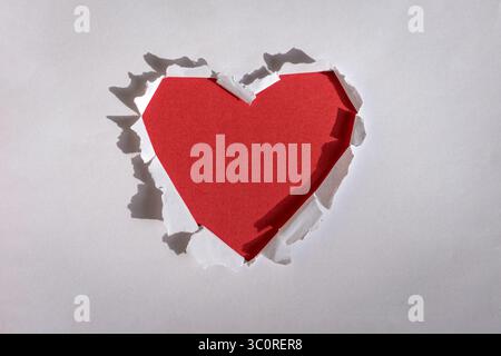 Rotes Loch in Herzform durch weißes Papier gerissen. Kopierbereich. Stockfoto