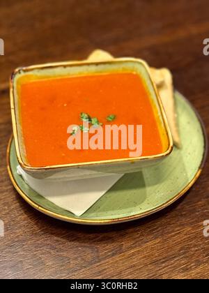 Schüssel mit heißer Tomatensuppe garniert mit Petersilie, serviert mit Toast auf einem rustikalen Holztisch. Stockfoto