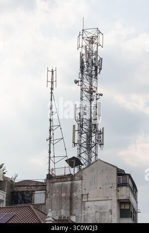 Ein großer Telekommunikationsturm mit mehreren Antennen steht auf dem Dach eines alten Gebäudes vor einem bewölkten Himmel. Stockfoto