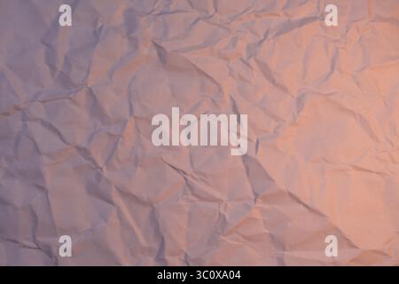 Eine zerknitterte weiße Papieroberfläche, die mit einem sanften Orange- und Violettton beleuchtet wird und einen stimmungsvollen Verlaufseffekt erzeugt. Ideal für abstraktes Design, Text-Overla Stockfoto