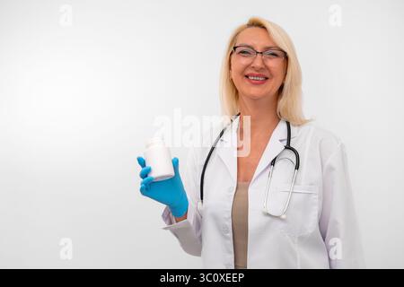 Zuversichtliche weibliche Ärztin im Labormantel und Handschuhe, die ein Glas Vitamine zeigen. Studio-Aufnahme, weißer Hintergrund mit Kopierraum Stockfoto