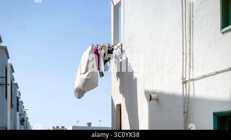 Ein modern gestaltetes Haus in weißer Farbe bei Tageslicht, eine Wand mit Kleidung hängt auf einem Wäscheständer. Stockfoto