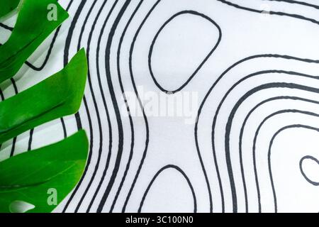 Stoffoberfläche mit abstrakten schwarzen Konturlinien und tropisch grünen Blättern. Perfekt für Hintergrund, Mockups oder modernes visuelles Design mit Natur. Stockfoto