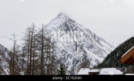 Schneebedeckte Berggipfel mit immergrünen Bäumen und einer malerischen Hütte im Winter Stockfoto