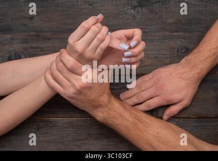 Die männliche Hand greift das weibliche Handgelenk auf dunkler Holzoberfläche fest und reflektiert Aggressionen, Spannungen und Angst. Physische Dominanz wird durch gewaltsam erfasst Stockfoto