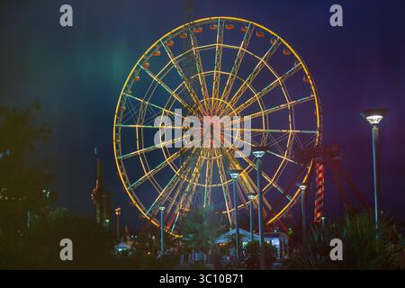 Ein großes, farbenfrohes Riesenrad leuchtet nachts auf. Die Lichter am Rad sind hell und farbenfroh und schaffen eine festliche Atmosphäre. Das Riesenrad ist Stockfoto