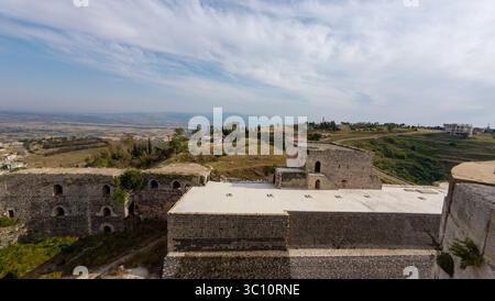 Aus der Vogelperspektive auf eine alte Steinfestung auf einem Hügel mit weitläufiger Landschaft und fernen Bergen unter einem teilweise bewölkten Himmel. Krak des Chevaliers Stockfoto