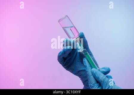 Arzthände in Handschuhen ziehen Impfstoff aus der Durchstechflasche in die Spritze Nahaufnahme auf rosa und blauem Hintergrund, Konzept der modernen Medizin Stockfoto
