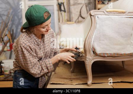 Frau ist mit der Restaurierung und Dekoration eines alten Vintage-Sofas beschäftigt. Möbelreparatur Stockfoto