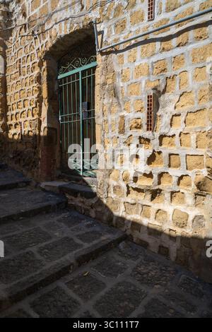Eine Nahaufnahme von oben zeigt die strukturierte Steinmauer und das kleine grün vergitterte Fenster eines historischen Gebäudes in Neapel, Italien. Stockfoto
