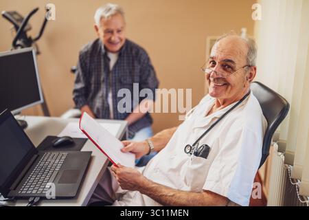 Der Senior-Mann macht eine Prüfung beim Kardiologen. Der Doktor sieht sich seine medizinischen Akten an. Glücklicher Arzt und Patient lächeln. Stockfoto