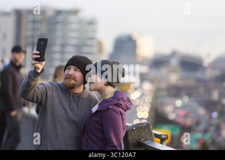 11. Januar 2019: Seattle, Washington, Vereinigte Staaten - Seattle, Washington: Ein Paar macht ein Selfie unter den Menschenmengen, die sich am Pike Place MarketFront versammelt haben, um den letzten Sonnenuntergang über dem Alaskan Way Viaduct zu erleben. Der Highway wurde am 11. Januar um 22 Uhr dauerhaft geschlossen, damit die Besatzungsmitglieder die State Route 99 vom Viadukt in einen hochmodernen Tunnel verlegen können. Die Doppeldeckerautobahn aus der Zeit von 1950â wurde beim Erdbeben von Nisqually 2001 schwer beschädigt und wurde lange über ihre Nutzungsdauer hinaus erhalten. Ein 3 km langer, langweiliger Straßentunnel ersetzt das Alaskan Way Viaduct, das die State Route 99 unter dem Sitz der Innenstadt führt Stockfoto