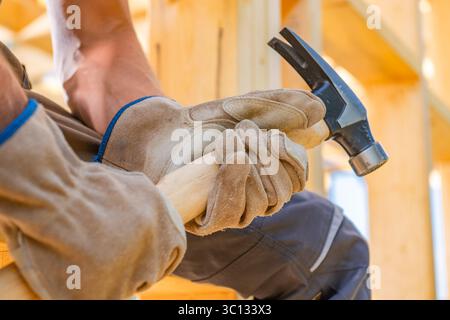 Ein Bauarbeiter mit Handschuhen schlägt tagsüber mit einem Hammer auf eine Holzplanke, um handwerkliches Können in Aktion zu zeigen. Stockfoto